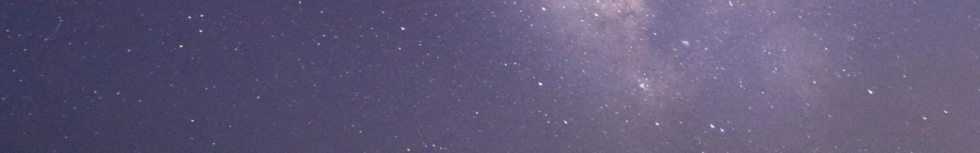 A softly lit sand dune in warm golden-brown tones rises under a vast purple-blue night sky filled with dense stars and the faint band of the Milky Way, creating a calm, expansive composition.